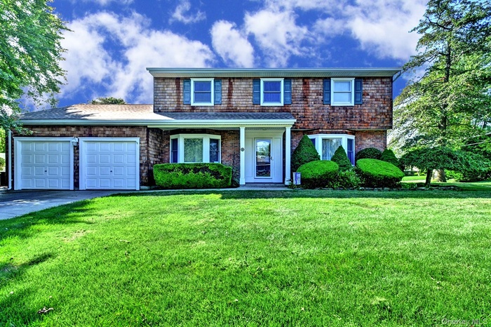 Traditional-style house with a garage, driveway, a front yard, and a porch