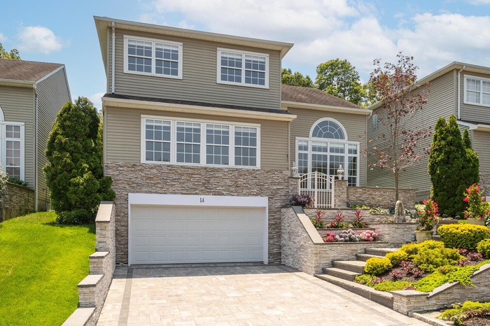 Traditional-style house with stone siding, a garage, driveway, and a front yard