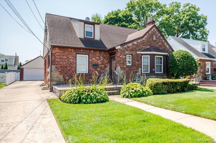 View of front facade with an outdoor structure, a detached garage, a front lawn, and a shingled roof