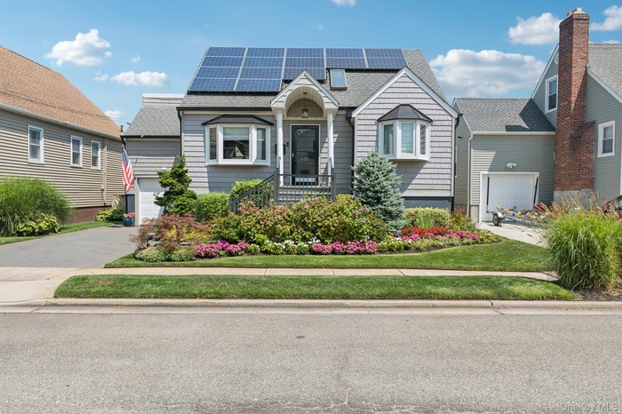 View of front facade featuring a shingled roof, roof mounted solar panels, and driveway
