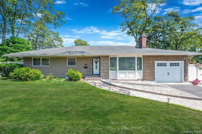 Ranch-style house featuring asphalt driveway, a shingled roof, an attached garage, a front lawn, and a chimney