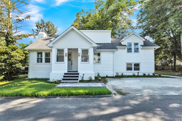 View of front of home featuring a chimney, a shingled roof, a porch, driveway, and a front yard