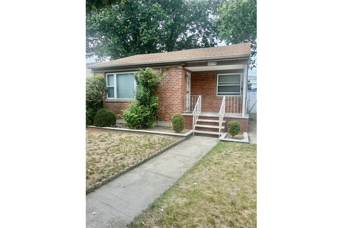 View of front of home with covered porch, brick siding, a front lawn, and roof with shingles