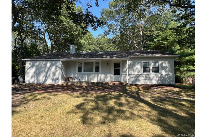 Ranch-style home with brick siding, covered porch, a chimney, and a front yard