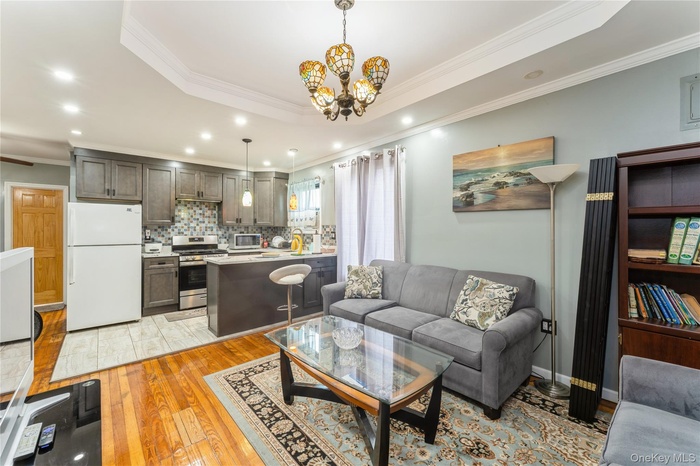 Living room featuring light wood-style flooring, ornamental molding, a tray ceiling, recessed lighting, and a chandelier