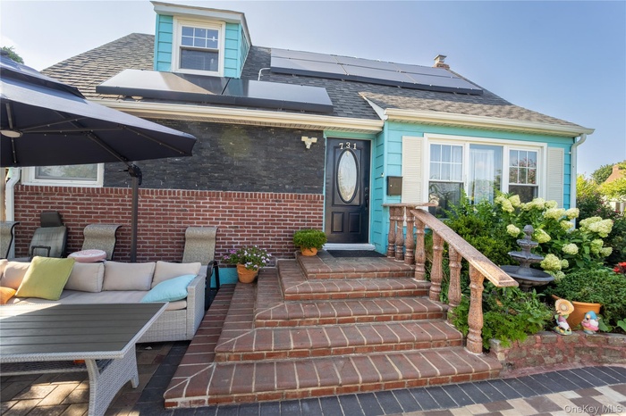 Doorway to property featuring roof mounted solar panels, an outdoor living space, a shingled roof, brick siding, and a patio