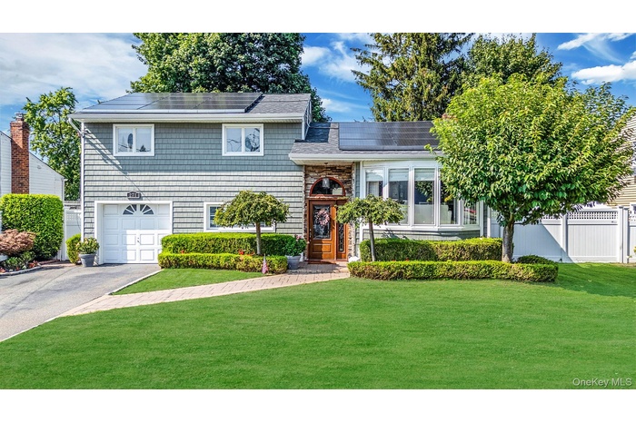 Split level home featuring roof mounted solar panels, an attached garage, asphalt driveway, and roof with shingles