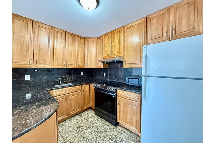 Kitchen with freestanding refrigerator, range with electric stovetop, under cabinet range hood, black microwave, and backsplash