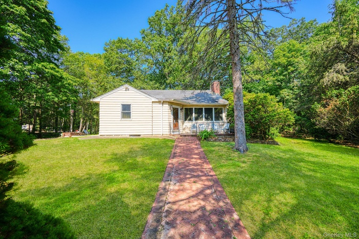 View of front of property featuring a sunroom, a chimney, and a front lawn