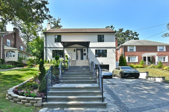 View of front of property featuring stucco siding, a chimney, stairs, decorative driveway, and a front lawn