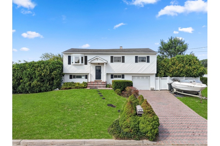 Bi-level home featuring decorative driveway, a garage, a chimney, and a shingled roof