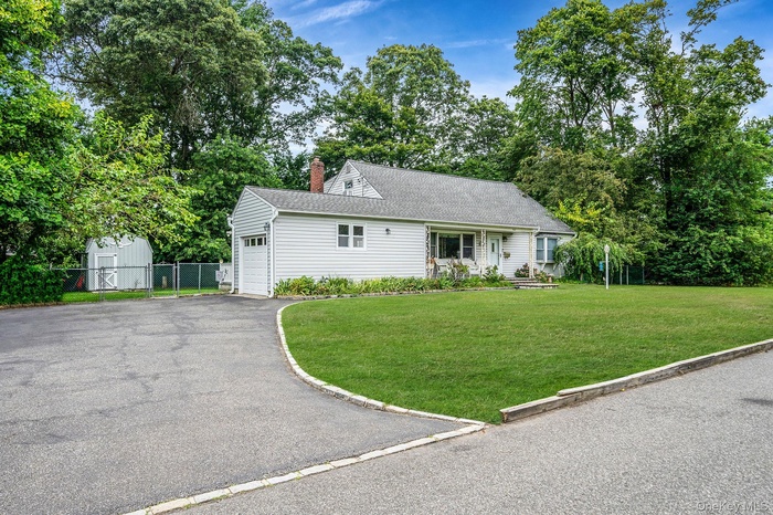 View of front facade with asphalt driveway, a garage, a chimney, view of scattered trees, and roof with shingles