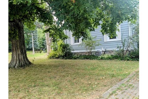 Attractive one and three quarter storey century old home on a corner lot, adorned with old maple trees and other green foliage in an expansive lawn.