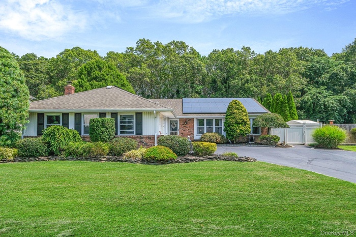 Ranch-style house featuring a gate, solar panels, brick siding, a chimney, and driveway