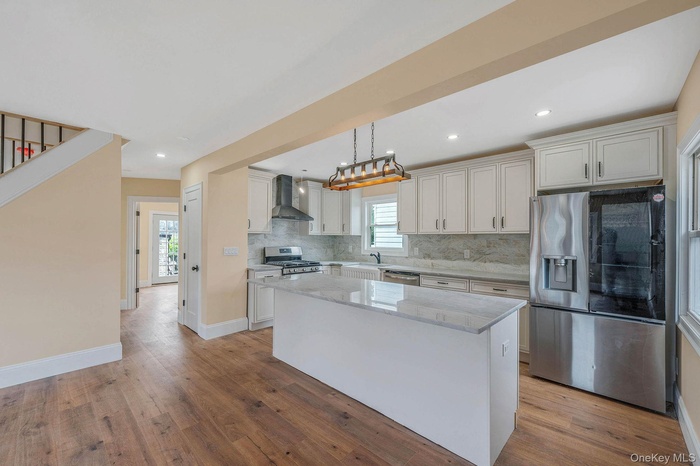 Kitchen featuring appliances with stainless steel finishes, wall chimney range hood, backsplash, a center island, and light wood finished floors