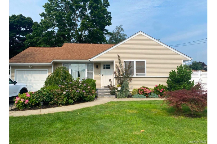 View of front of property featuring an attached garage, a front lawn, and roof with shingles
