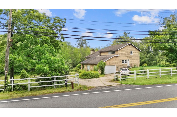 View of front of property featuring driveway, a chimney, and a shingled roof