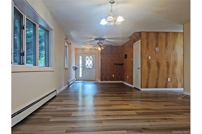 living room with wood walls, a baseboard heating unit, wood finished floors, a chandelier, and a ceiling fan