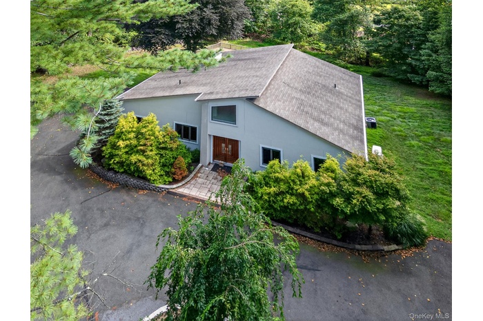 View of front of home with roof with shingles, stucco siding, and view of wooded area