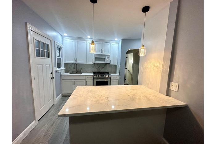Kitchen with dark wood-style floors, a sink, stainless steel range with gas cooktop, white microwave, and arched walkways