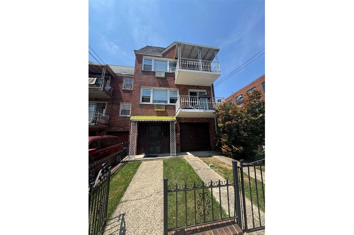 View of front of house featuring a balcony, brick siding, a fenced front yard, and an attached garage