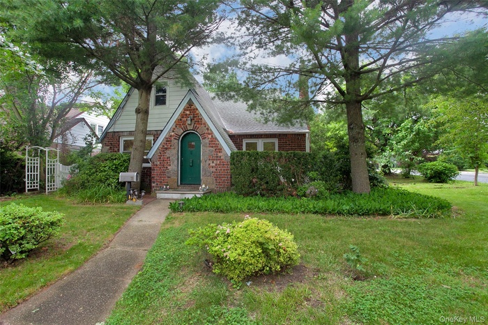 Tudor home featuring brick siding, a front yard, and roof with shingles