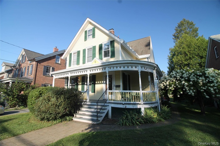 View of front of house with a porch, a front yard, and a shingled roof