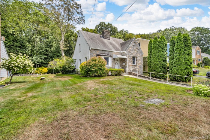 View of front of home with stone siding, a chimney, a front lawn, and a shingled roof