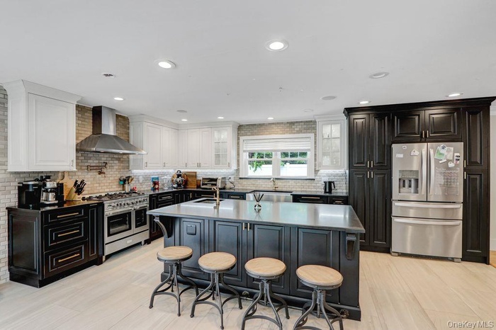 Kitchen featuring appliances with stainless steel finishes, decorative backsplash, wall chimney exhaust hood, a breakfast bar area, and recessed light