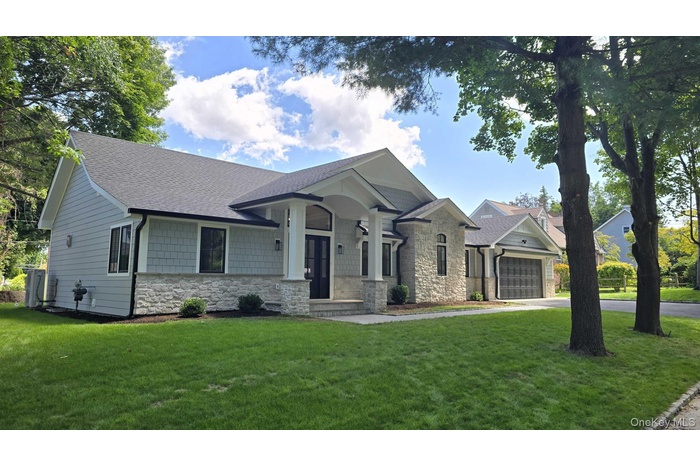 View of front of property with stone siding, a garage, a front lawn, and a shingled roof