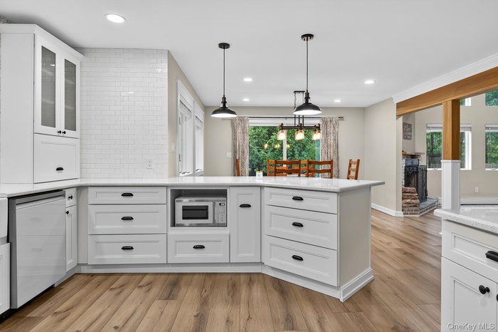 Kitchen with white cabinets, light stone countertops, glass insert cabinets, decorative light fixtures, and recessed lighting