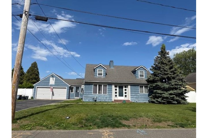 Cape cod house featuring driveway, a chimney, a garage, and a front lawn