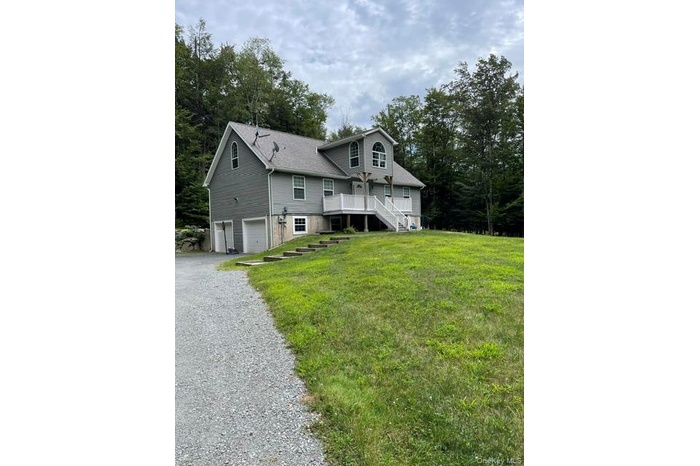 View of front of home with a garage, driveway, stairs, a front yard, and a wooden deck