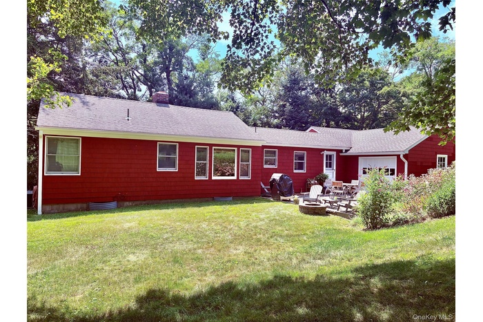 Back of house featuring a fire pit, a patio, roof with shingles, a chimney, and a lawn