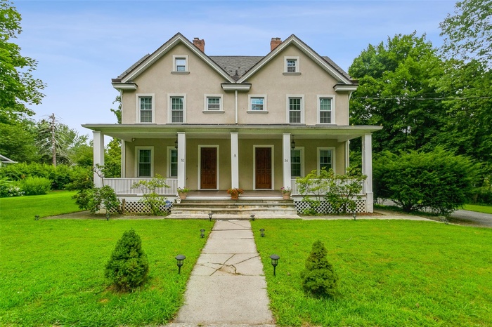 View of front facade featuring stucco siding, a porch, a front lawn, and a chimney