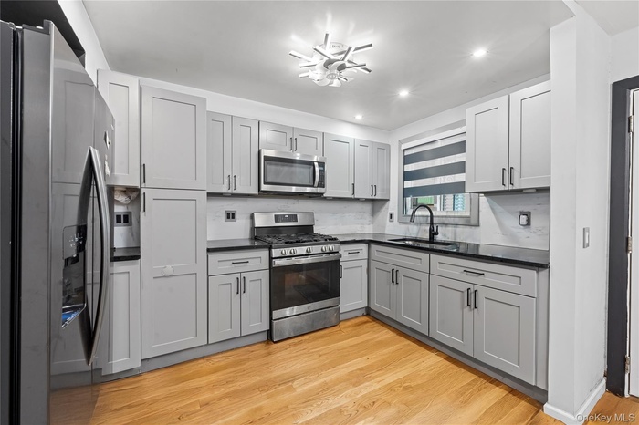 Kitchen with stainless steel appliances, light wood-style flooring, gray cabinetry, backsplash, and recessed lighting