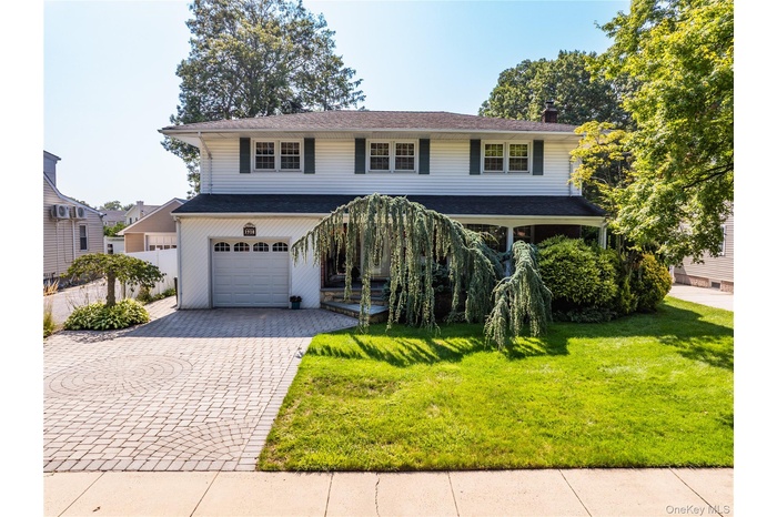 Front facade with decorative driveway, a front yard, an attached garage, a chimney, and a porch