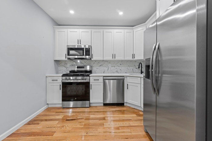 Kitchen with stainless steel appliances, a sink, light countertops, white cabinetry, and recessed lighting