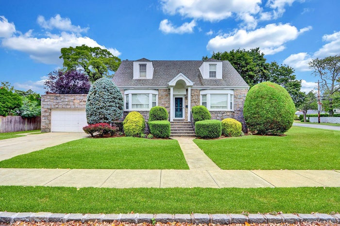 Cape cod house featuring stone siding, a shingled roof, concrete driveway, and an attached garage