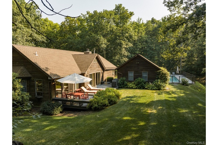 Rear view of property featuring a deck, a chimney, a lawn, and roof with shingles