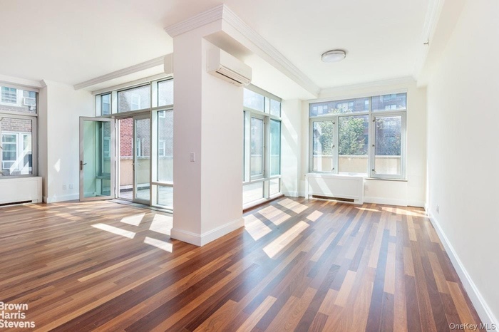 Empty room featuring crown molding, wood finished floors, a wall mounted AC, and radiator heating unit