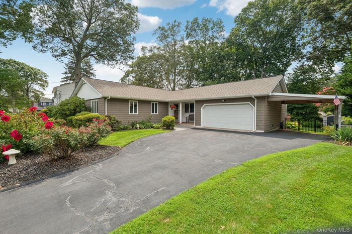Ranch-style house with a shingled roof, an attached garage, an attached carport, and asphalt driveway