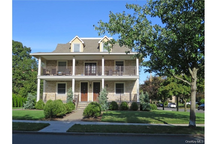 View of front of home with a porch, a front lawn, stone siding, and a shingled roof