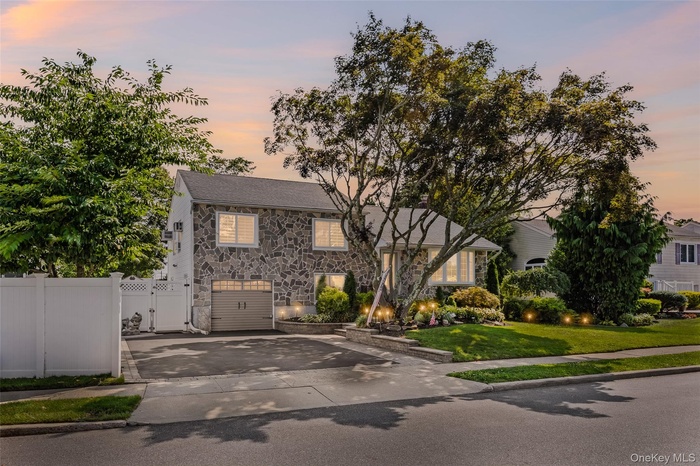 View of front facade with stone siding, concrete driveway, a gate, and an attached garage