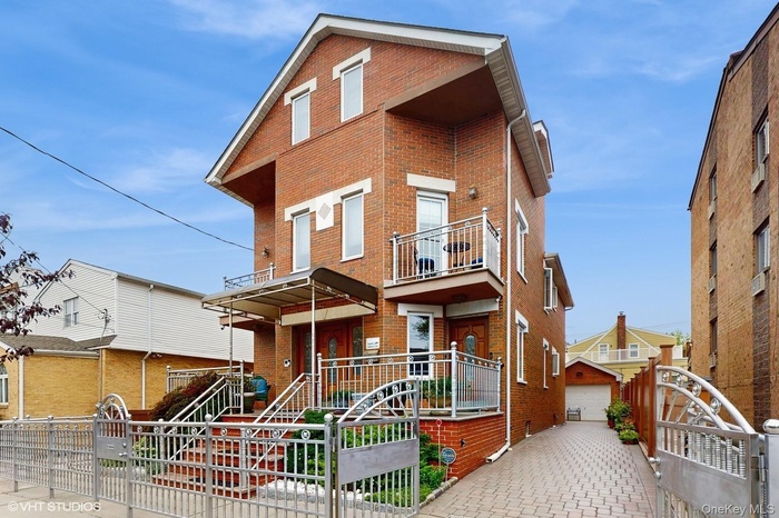View of front of house featuring brick siding, an outdoor structure, a gate, a balcony, and a fenced front yard