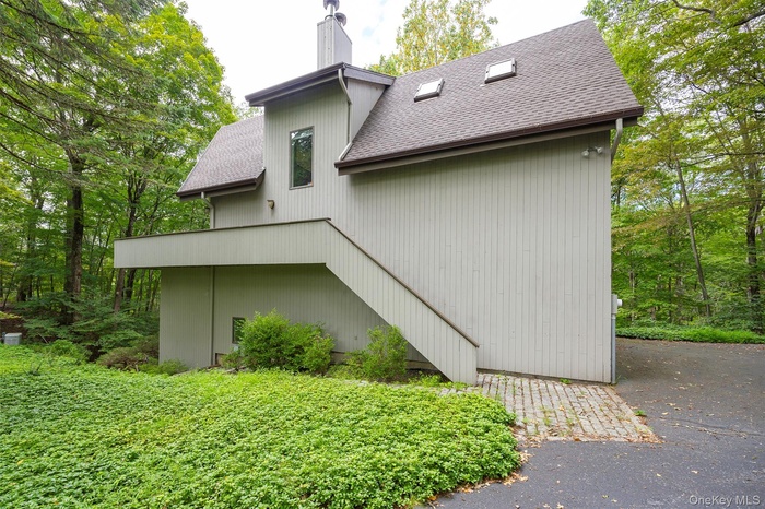 Back of property with a chimney, roof with shingles, and driveway