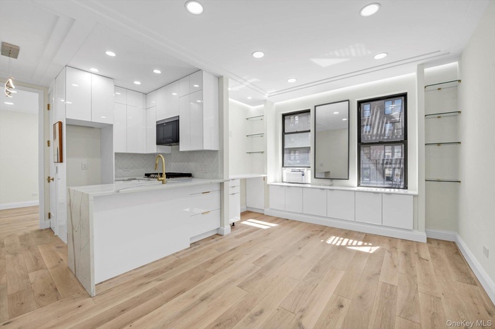 Kitchen with modern cabinets, white cabinets, light stone countertops, tasteful backsplash, and light wood finished floors