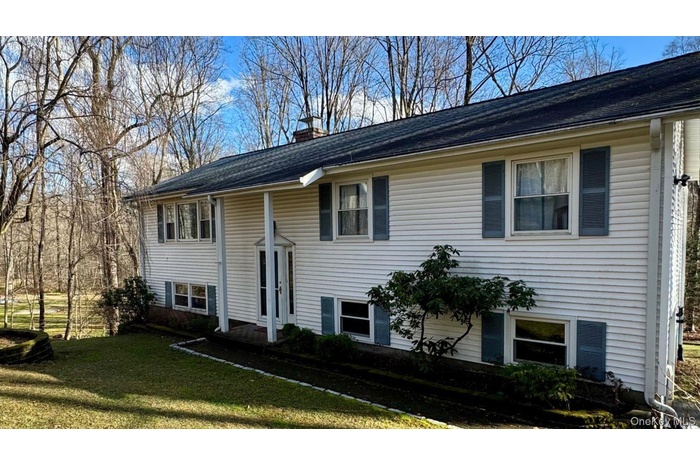 Split foyer home featuring a chimney, a front yard, and roof with shingles