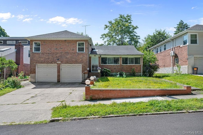 Split level home with an attached garage, driveway, brick siding, a front yard, and a shingled roof