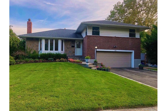 Tri-level home featuring asphalt driveway, an attached garage, a lawn, and a chimney